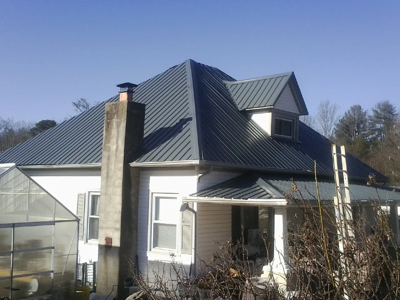Dark blue standing seam metal roof on a white farmhouse with dormer — Slate & Tile Roof Repair by Roofing Brothers in Schwenksville