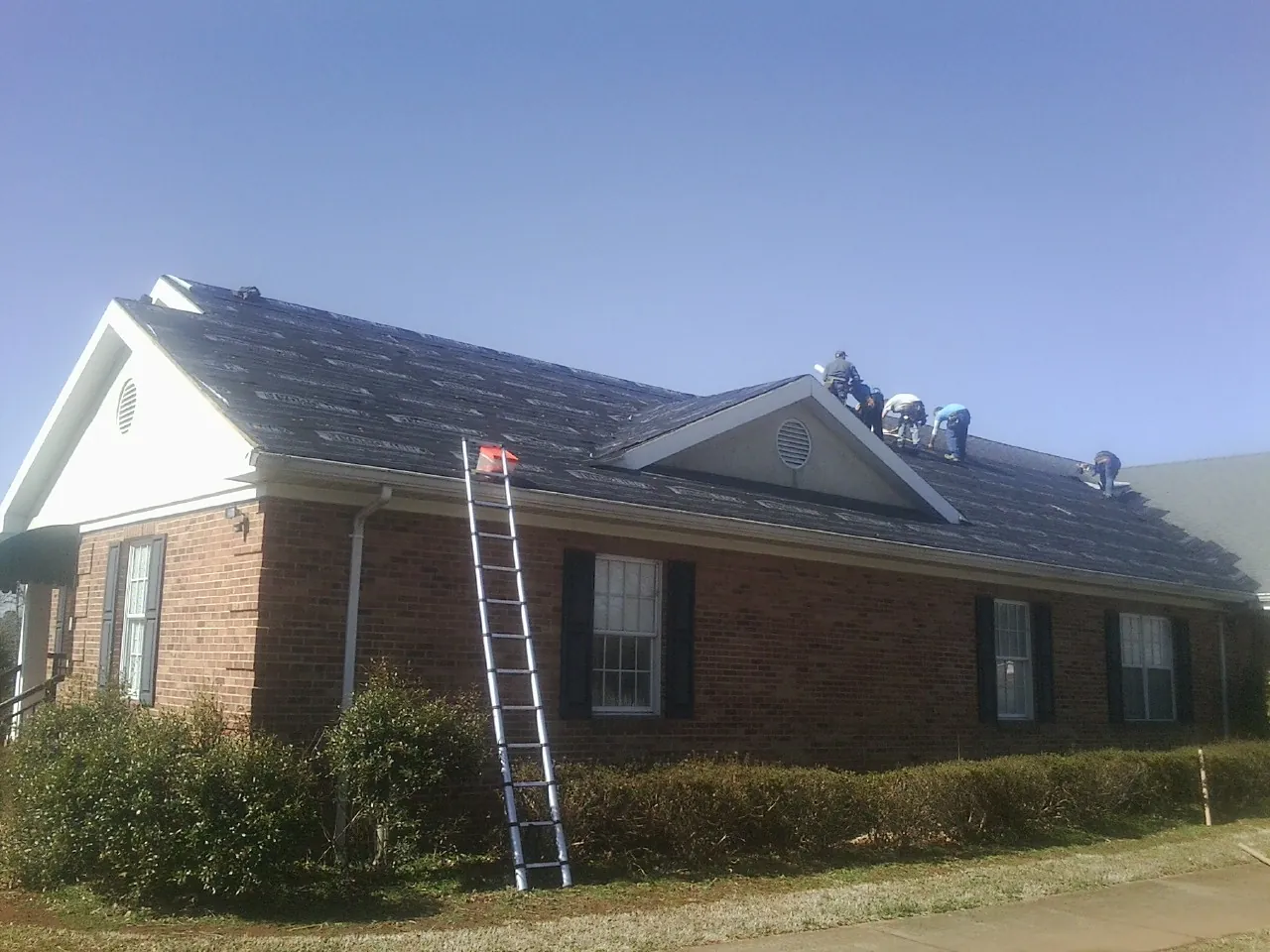 Crew tearing shingles off a brick ranch roof with a ladder set — Emergency Roof Repair work by our crew in Schwenksville