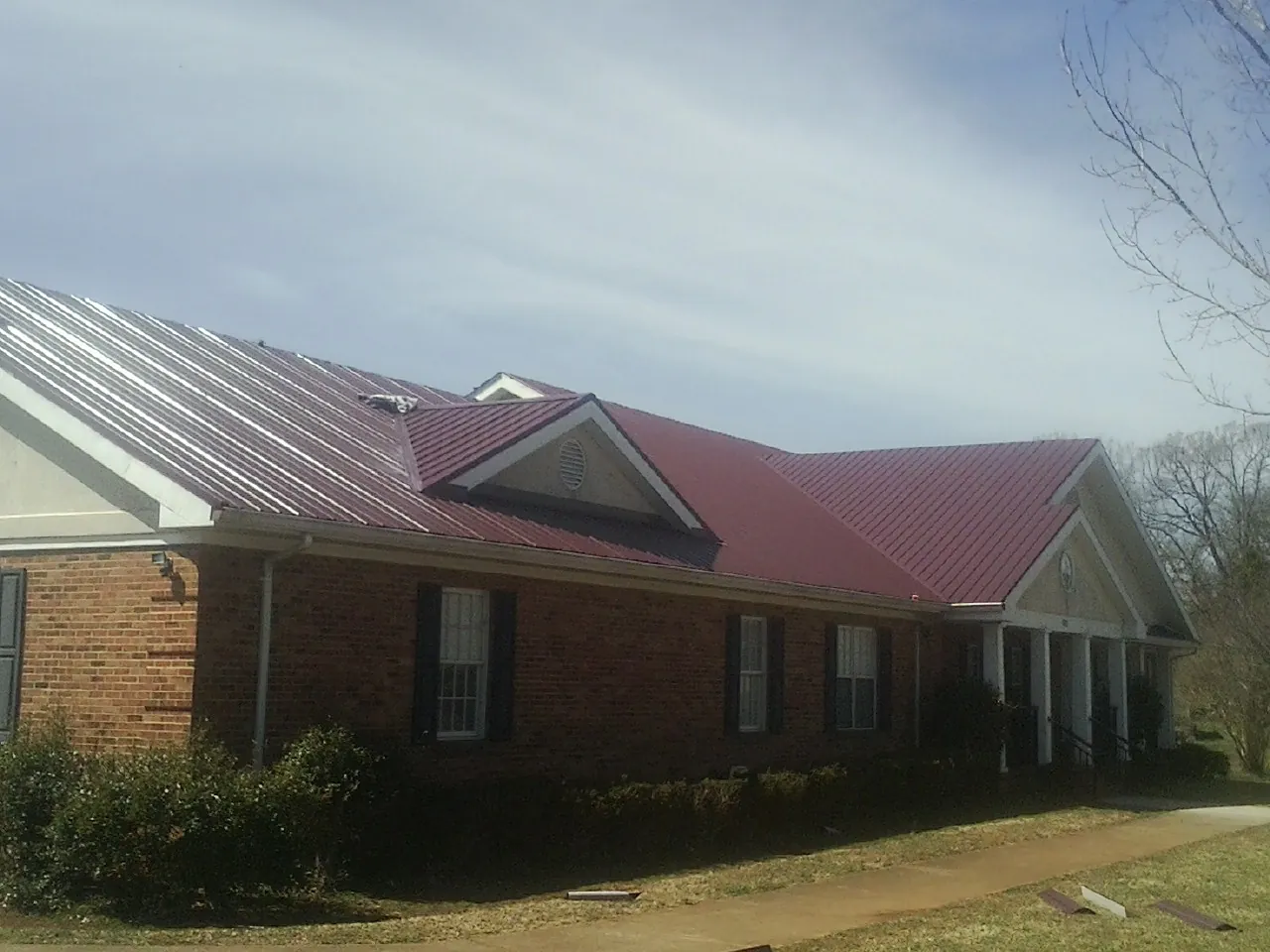 Red metal roof with gabled entries on a long brick building, from a Hail Damage Roof Repair job in Schwenksville