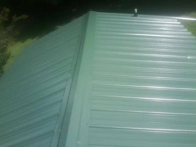 New green metal panels meeting at the ridge of a roof — Flat Roof Repair work by our crew in Schwenksville
