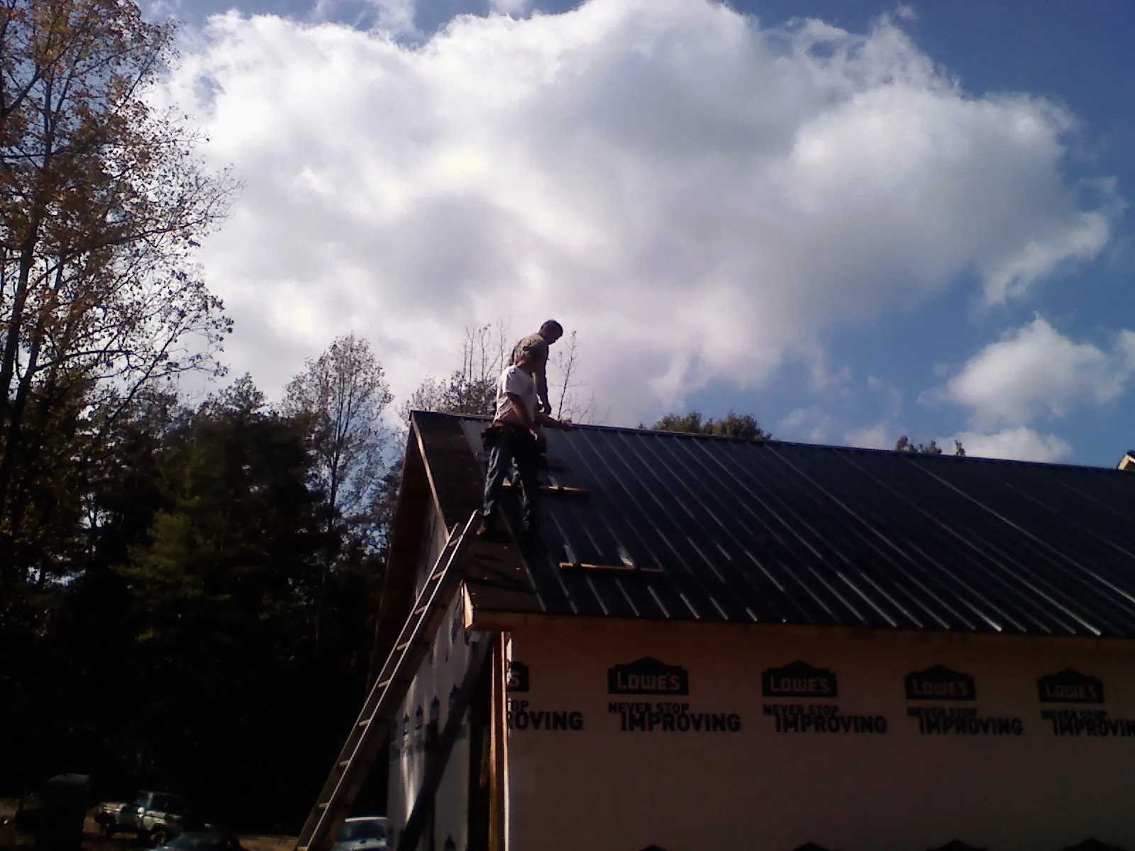 Roofer fastening dark metal panels high against a cloudy sky, from a Roof Inspection job in Schwenksville