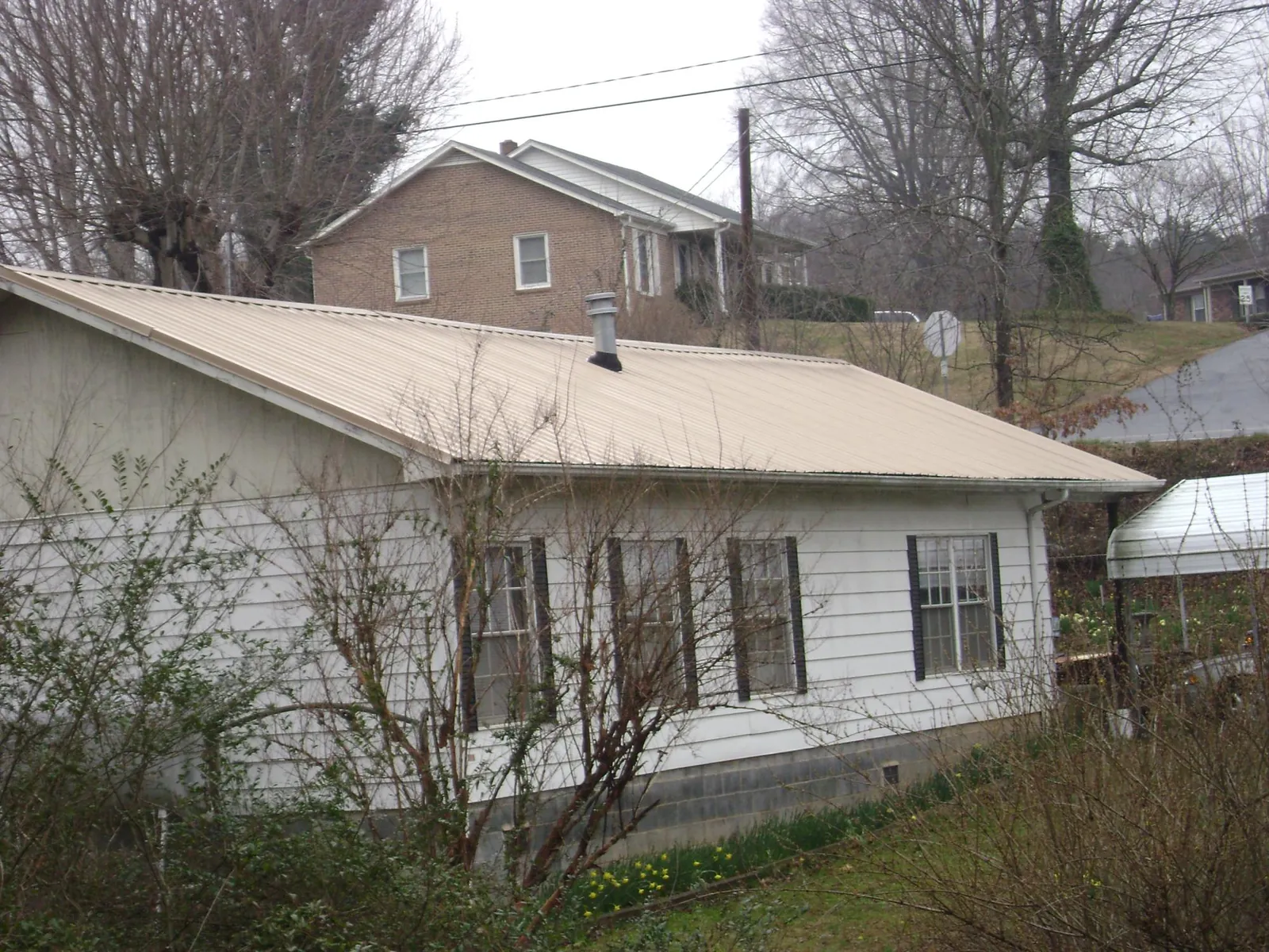 Tan metal roof on a white sided house set into a hillside — Commercial Roofing by Roofing Brothers in Schwenksville
